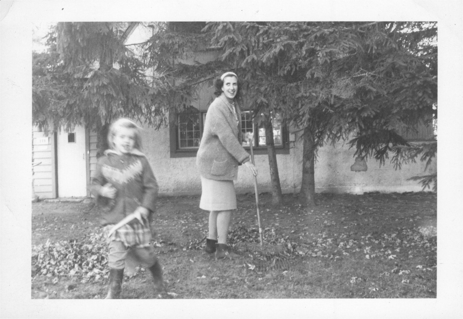Woman raking leaves with child in garden, 1950s