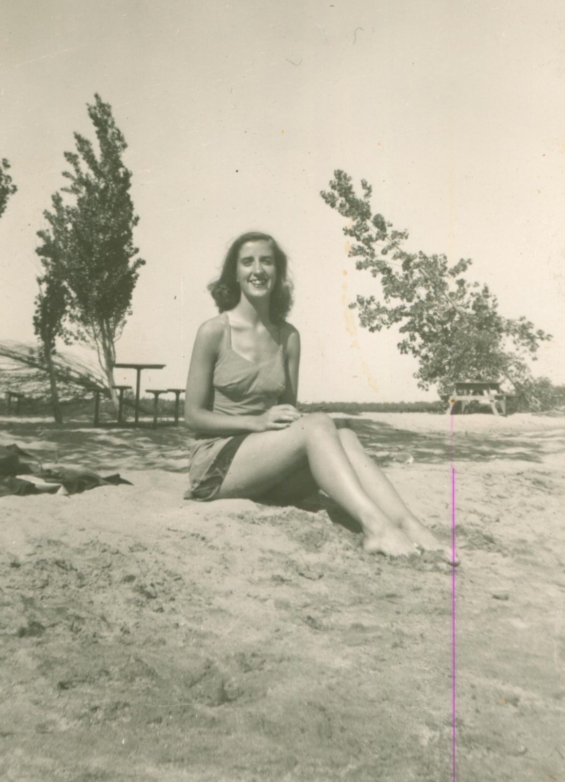 Young woman sitting on beach, 1940s